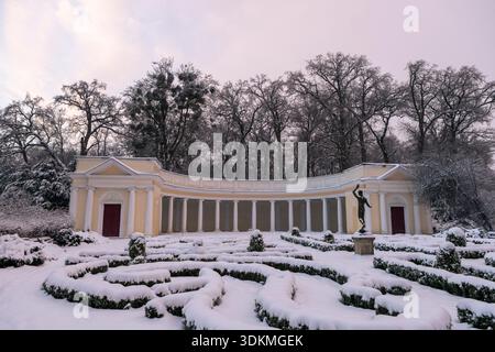 Dans un arboretum hivernal serein, des monuments architecturaux se dressent parmi les arbres recouverts de neige. Les chutes de neige douces des branches renforcent l'atmosphère élégante Banque D'Images