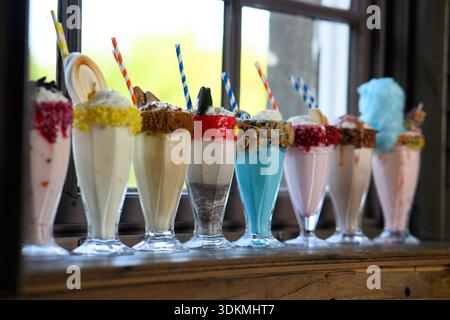 Une rangée de milkshakes colorés avec des pailles dedans. Les milkshakes sont en rangée sur un rebord de fenêtre Banque D'Images