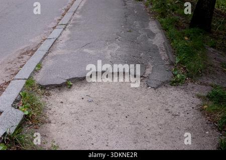 Chemin d'asphalte brisé avec de l'herbe verte et la partie inférieure d'un tronc d'arbre visible sur le côté. Banque D'Images