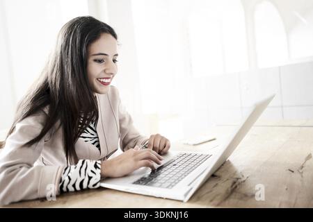 Blithe Serenity pendant le travail en ligne numérique, une femme dans un blazer beige souriant comme elle tape sur un ordinateur portable ou macbook, l'air joyeux excité a Banque D'Images