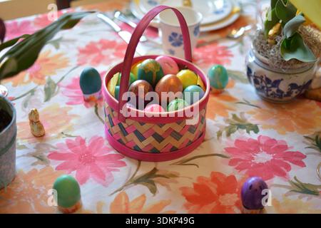 Petit panier tissé rempli d'œufs de Pâques colorés placés sur une table à manger printanière festive. Banque D'Images