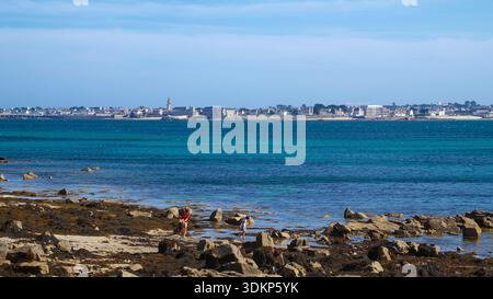 Une côte rocheuse accidentée avec vue sur la mer ouverte et une ville lointaine skyline à l'horizon, le tout sous un ciel bleu vif. Banque D'Images