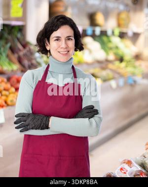 Employé de magasin de femme dans le tablier et les stands de gants dans la zone de vente de légumes Banque D'Images