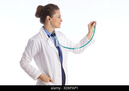 Une femme médecin d'âge moyen portant une blouse de laboratoire blanche et une cravate bleue tient une pièce de poitrine de stéthoscope, montrant à nouveau une attention concentrée et une expertise médicale Banque D'Images