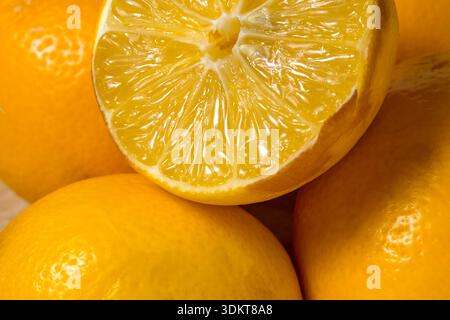 Plusieurs citrons reposent sur une surface en bois, avec un citron coupé en deux pour révéler la chair jaune. La couleur vive du fruit montre la fraîcheur et mûre Banque D'Images