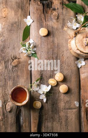 Service à thé traditionnel avec théière en verre et tasse sur une table en bois rustique décorée de fleurs de jasmin blanc et de boules de mochi vue de dessus Banque D'Images