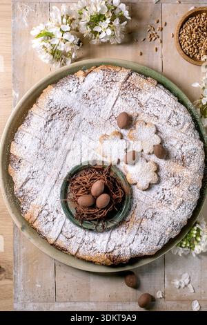 Gâteau rond fait maison Pastiera Napolitano saupoudré de sucre en poudre décoré de chocolat oeufs nid pièce maîtresse fleur découpe biscuits fleur de printemps Banque D'Images