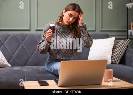 Jeune femme est assise sur le lit dans le salon et ayant rendez-vous en ligne du médecin à l'aide d'un ordinateur portable. Consultation à distance avec le médecin. Banque D'Images