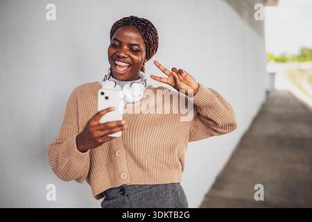 Portrait extérieur de la jeune femme noire qui écoute selfie avec smartphone. Banque D'Images