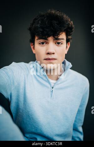 Jeune homme sérieux en pull bleu clair sur fond sombre Banque D'Images