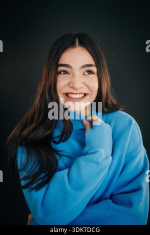 Riant jeune femme en sweat-shirt bleu vif sur fond sombre Banque D'Images