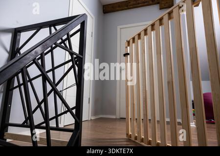 Espace intérieur avec escalier en métal noir, portail en bois clair, plancher en bois poli, murs gris, portes blanches, et une poutre de plafond en bois. Banque D'Images