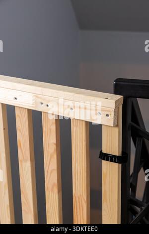 Une vue détaillée d'une barrière de sécurité en bois avec des lattes verticales, fixées par des vis, avec un loquet en plastique noir sur un cadre en métal noir à l'intérieur. Banque D'Images