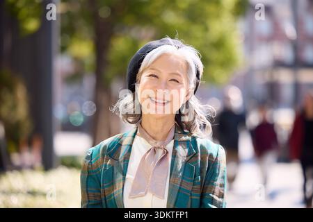 Femme senior souriante en veste à carreaux et béret Japon Banque D'Images