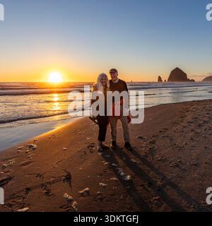 États-Unis, Oregon, Cannon Beach, Portrait de couple senior souriant sur la plage avec rocher de meule de foin en arrière-plan Banque D'Images