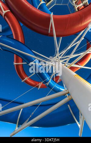 Vue d'un tourbillon vertigineux de toboggans d'eau rouges et bleus tournant contre un ciel bleu vibrant, capturé sous un angle bas, Izola, Slovénie. Banque D'Images
