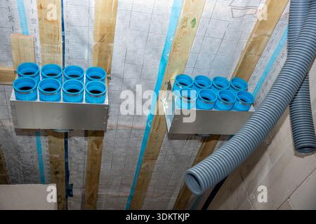 Composants d'un système de ventilation à récupération de chaleur avec des conduits bleus et des tuyaux gris montés sur des poutres en bois dans une structure de plafond exposée. Banque D'Images