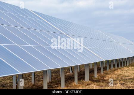 Grand panneau solaire sur cadres métalliques dans un champ avec de l'herbe sèche et du sol, placé contre un ciel couvert avec un éclairage diffus. Banque D'Images