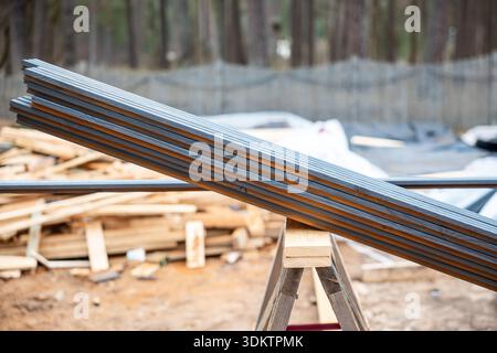 Chantier de construction avec poutres métalliques sur un sawhorse en bois, matériaux dispersés, et une clôture en maille avec une zone boisée en arrière-plan. Banque D'Images