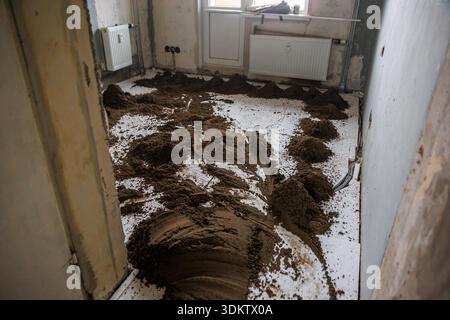 Chambre en rénovation avec sol meuble sur sol carrelé blanc, murs inachevés, tuyaux exposés, radiateur et lumière naturelle entrant par une fenêtre. Banque D'Images