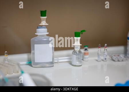 Installation médicale sur un comptoir blanc avec bouteilles, ampoules, flacons et seringues disposés dans un environnement clinique contre un mur beige. Banque D'Images
