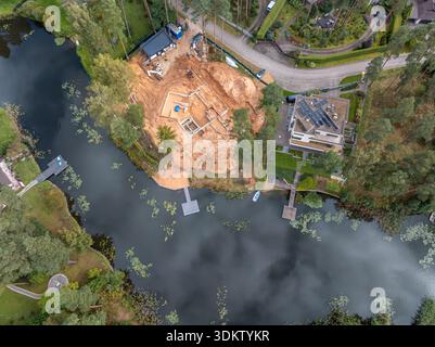 Une vue aérienne montre un chantier de construction sur une péninsule entourée d'eau, une maison moderne avec des panneaux solaires, un quai en bois, des arbres et un veget aquatique Banque D'Images