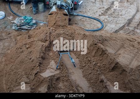 Un chantier de construction montrant un tas de sable avec des traces de pneus, une brouette, un malaxeur de béton, des tuyaux et des outils et matériaux dispersés. Banque D'Images
