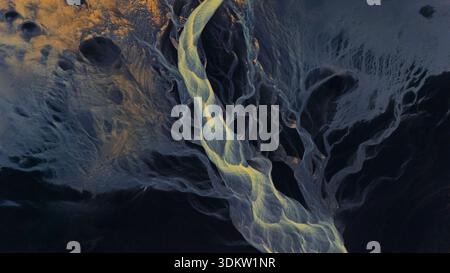 Vue aérienne des canaux de rivière tressés creusent à travers le paysage sombre et contrasté, une symphonie d'or contre le bleu profond, Selfoss, Islande. Banque D'Images