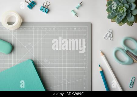 Fond de papeterie avec cahier turquoise et ciseaux à la menthe sur tapis de découpe gris. Espace de travail organisé avec espace de copie. Banque D'Images