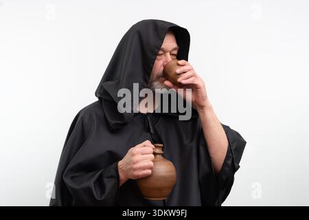 Moine mature barbu avec hotte buvant la boisson de la tasse en céramique dans le studio Banque D'Images