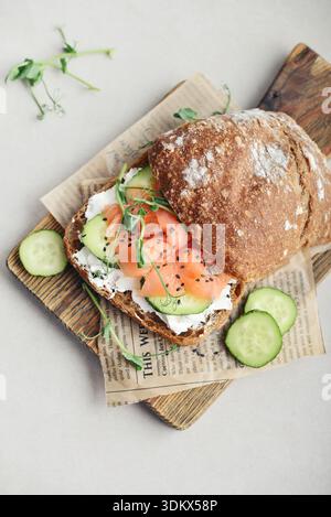 Sandwich au pain de seigle avec saumon salé, concombre, légumes verts et fromage à la crème sur planche à découper en bois gros plan Banque D'Images