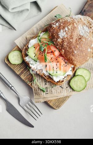 Sandwich au pain de seigle avec saumon salé, concombre, légumes verts et fromage à la crème sur planche à découper en bois gros plan Banque D'Images