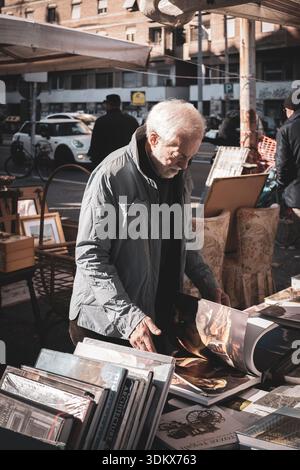 Vieil homme feuilletant des artbooks au marché aux puces de Porta Portese, Rome, Italie Banque D'Images