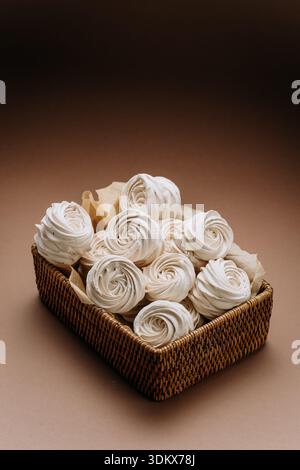 Rosettes meringues blanches dans un panier en osier sur fond beige, espace copie Banque D'Images