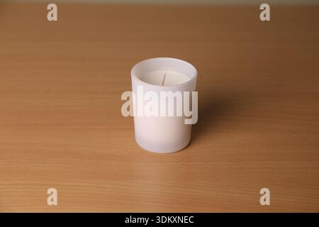 Une bougie blanche est placée sur une table en bois. Il se trouve dans un support transparent avec une seule mèche. La lumière naturelle remplit la pièce, créant un cadre calme pour re Banque D'Images