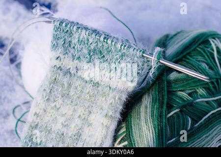 Chaussettes tricotées avec aiguilles à tricoter sur neige. Chaussettes dégradées blanches et vertes. Mode tricoté. Chaussettes chaudes en laine avec aiguilles à tricoter. Passe-temps de tricot. Banque D'Images