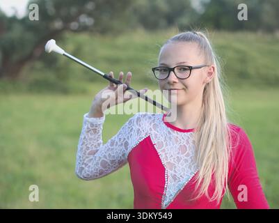 Teen blonde à lunettes fille Majorette Twirling Baton en plein air en robe rouge Banque D'Images