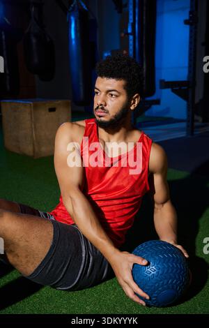 Un jeune homme afro-américain exerce avec concentration, en utilisant un medecine ball à l'intérieur. Banque D'Images