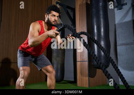 Un jeune sportif afro-américain dévoué se concentre sur son entraînement en utilisant des cordes de combat à l'intérieur. Banque D'Images