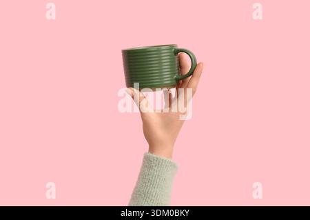 Main femelle avec tasse en céramique verte sur fond rose Banque D'Images