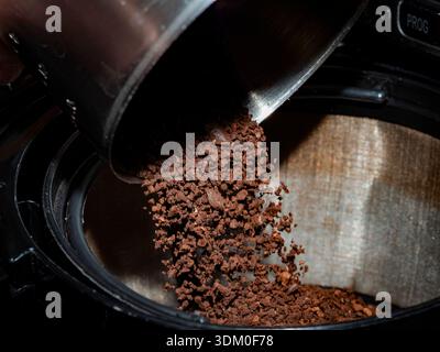 Plan d'action de café moulu torréfié foncé versé à partir d'une pelle en acier inoxydable dans un panier à filtre à café en maille. Banque D'Images