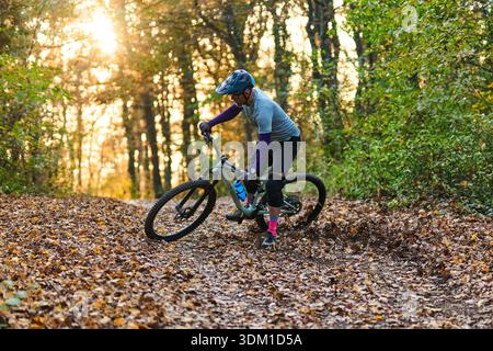Le VTT navigue sur le sentier forestier couvert de feuilles pendant le coucher du soleil doré Banque D'Images