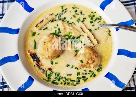 Soupe au fromage avec boulette de bacon et nouilles célestyne dans une assiette blanche à rayures bleues, gros plan. Banque D'Images