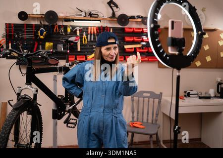 Femme blogueuse influencer live streaming travaillant dans garage, vlogger faisant geste main invitant à venir. mécanicien de vélo dans les petites entreprises. bricoleur Banque D'Images