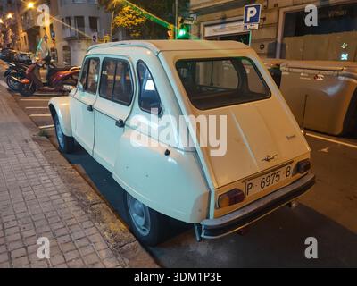 Vue arrière d'une vieille voiture classique garée dans les rues de la ville de Barcelone la nuit. La mythique Citroën 2CV Dyane 6 de couleur crème Banque D'Images