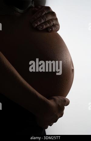 Profil de silhouette du ventre d'une femme enceinte sur un fond blanc brillant. Gros plan de la future mère qui la tient Banque D'Images
