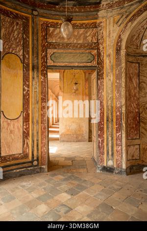 AGLIÈ, ITALIE – OCTOBRE 2025 : vue intérieure du château d'Agliè montrant des murs peints ornés, des textures de marbre vieilli et des portes menant à un corrido ensoleillé Banque D'Images