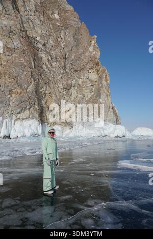 Femme en vêtements d'hiver chauds se tient sur la glace claire près des falaises gelées massives du lac Baïkal sous le ciel bleu vif Banque D'Images