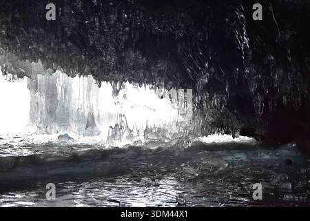 Grotte de glace gelée sur le lac Baïkal en hiver, des glaçons imposants et des murs de glace lisses formant une chambre naturelle spectaculaire le long du rivage rocheux. Banque D'Images