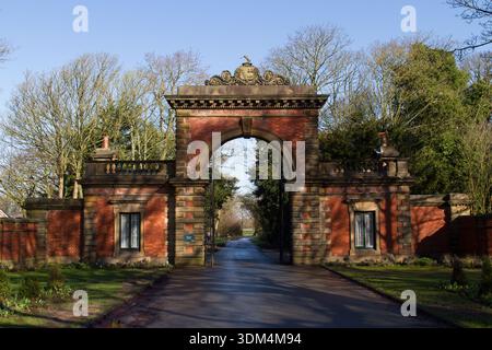 Porte d'entrée en briques historique à Lytham Hall, Lancashire, Royaume-Uni, encadrée par des arbres par une journée ensoleillée avec une allée menant à travers l'arche. Banque D'Images